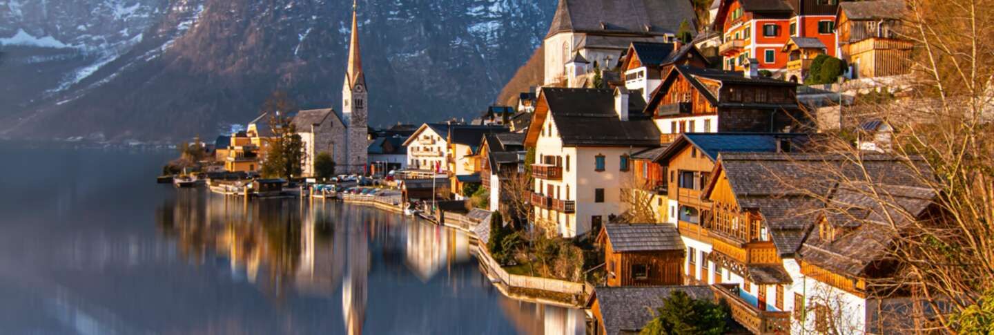 עיירה באוסטריה לצד אגם, עם בתים מסורתיים, הרים מושלגים ברקע וכנסייה גבוהה 