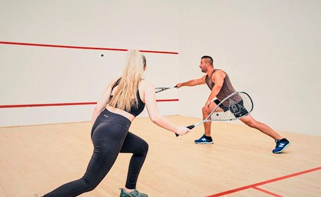 אישה וגבר משחקים סקווש באולם סגור במלון לאונרדו The Dilly בלונדון 