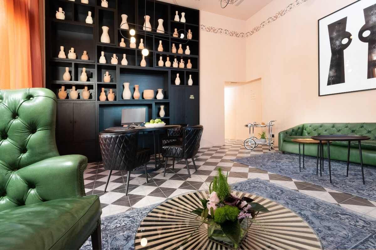 אזור קבלה במלון בכר האוס עם ספה וכורסה ירוקות, ספרייה שחורה עם כלי חרס ורצפת אריחים שחור לבן