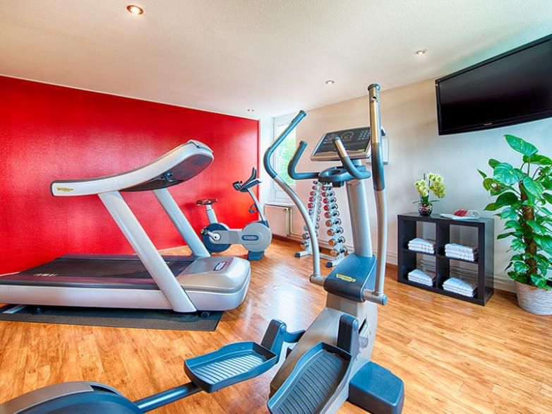 חדר כושר במלון לאונרדו המבורג סיטי נורד עם מסלול ריצה, מכשירי כושר, משקולות וטלוויזיה על הקיר
