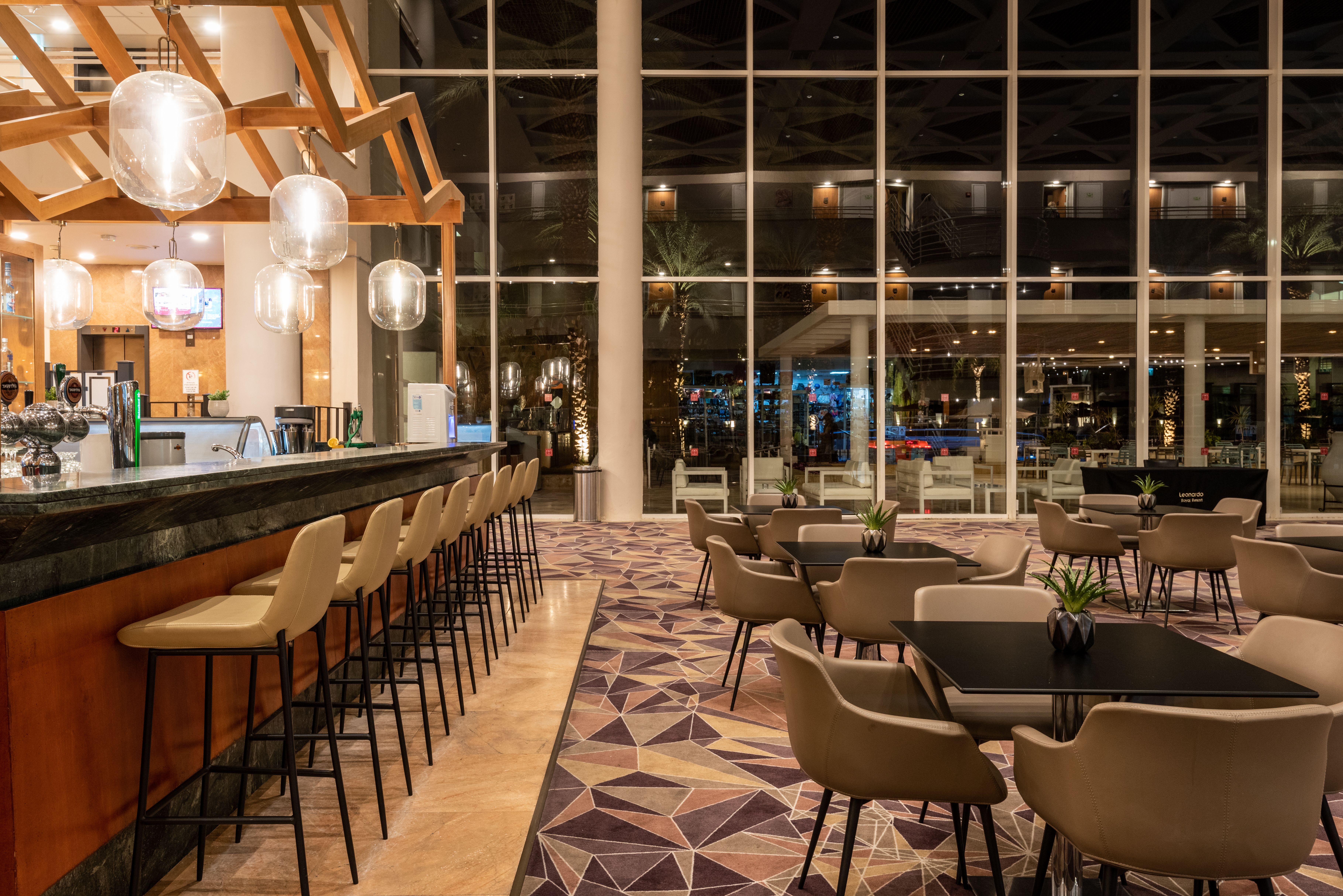 בר יוקרתי ומעוצב במלון לאונרדו רויאל ריזורט אילת, עם תאורה חמימה וריהוט מודרני בצבע בז'