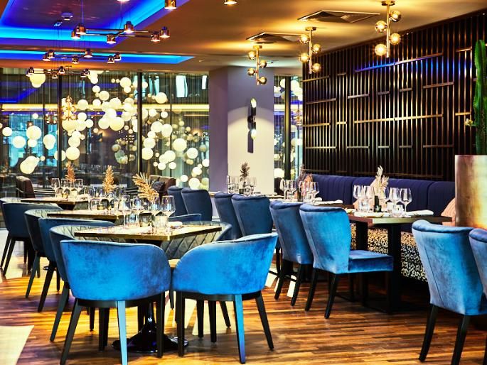 מסעדה במלון NYX וורשה, מעוצבת באווירה מודרנית עם כיסאות קטיפה כחולים ושולחנות ערוכים 