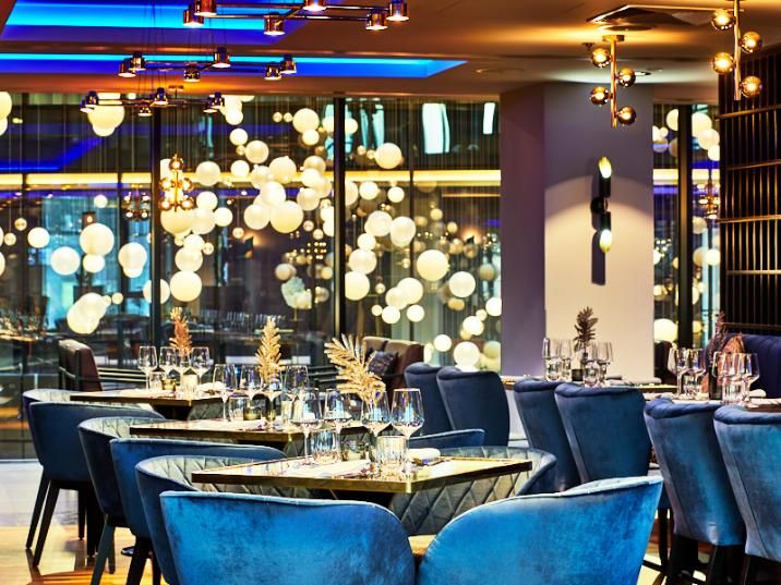 מסעדה אלגנטית במלון NYX וורשה עם כיסאות קטיפה כחולים, שולחנות ערוכים ותאורה מרהיבה של כדורים מוארים