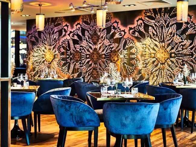 פינת ישיבה יוקרתית במלון NYX וורשה עם כיסאות קטיפה כחולים וקיר בעיצוב פרחוני דרמטי