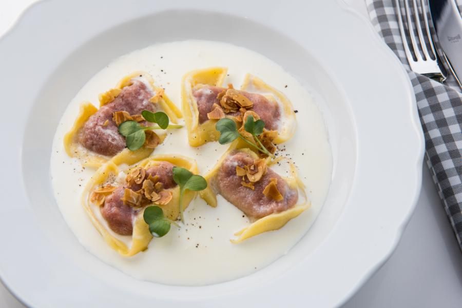 רביולי במילוי סלק ברוטב שמנת, בתוספת פרוסות שקדים וירק טרי על צלחת לבנה