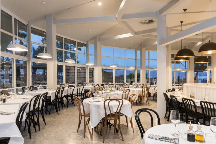 מסעדה אלגנטית עם שולחנות ערוכים ומפות לבנות, חלונות פנורמיים ונוף לים