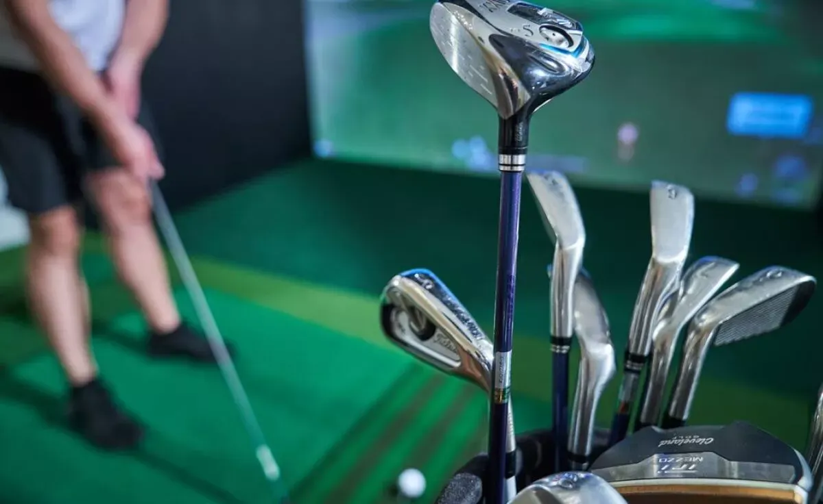 אדם עומד במרחק כשהוא אוחז במקל גולף, ברקע מסך סימולציה של מגרש גולף