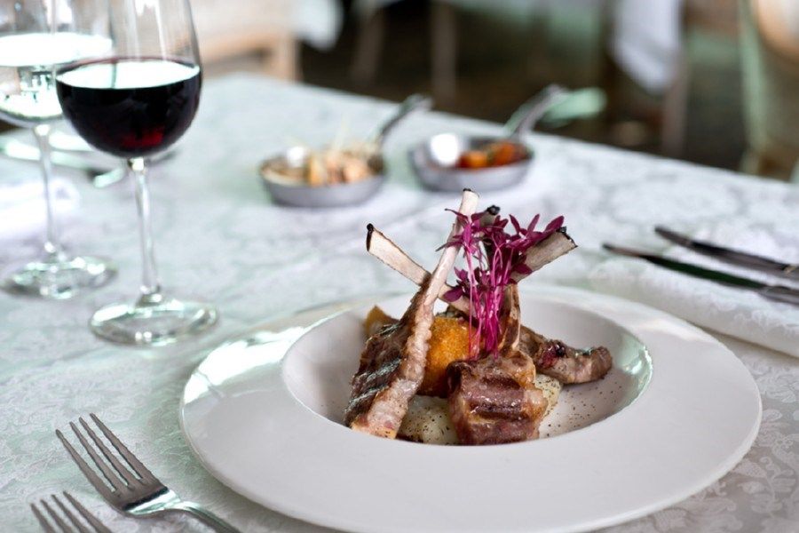 צלעות טלה מוגשות על צלחת לבנה לצד כוס יין אדום