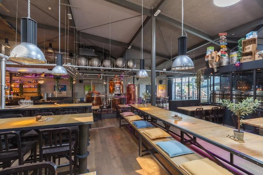 מסעדת בירה במלון לאונרדו אלמרה סנטר, עם שולחנות עץ ארוכים, תאורה תעשייתית ובר משקאות מפואר