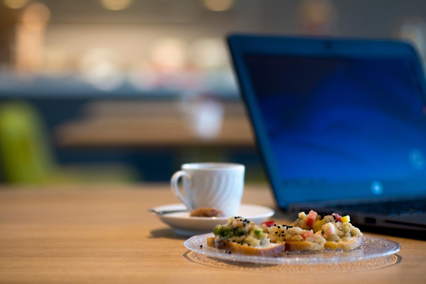  שולחן עם קפה, פרוסות לחם עם ממרח על צלחת זכוכית ולפטופ