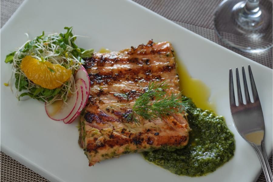 מנה של סלמון צלוי עם רוטב עשבי תיבול, מוגשת לצד סלט טרי עם צנונית ופלח תפוז