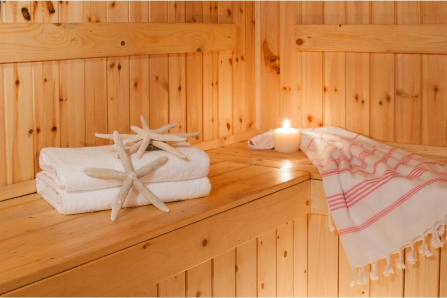  סאונה מעץ בה מונחות מגבות נקיות, צדפים דקורטיביים ונר דולק