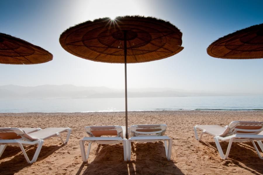 כיסאות שיזוף ושמשיות על חוף הים עם נוף למפרץ אילת