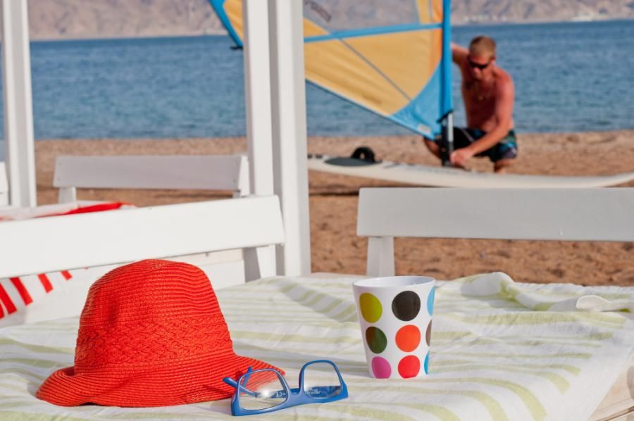 כובע אדום, כוס צבעונית ומשקפיים כחולים על מיטת שזוף