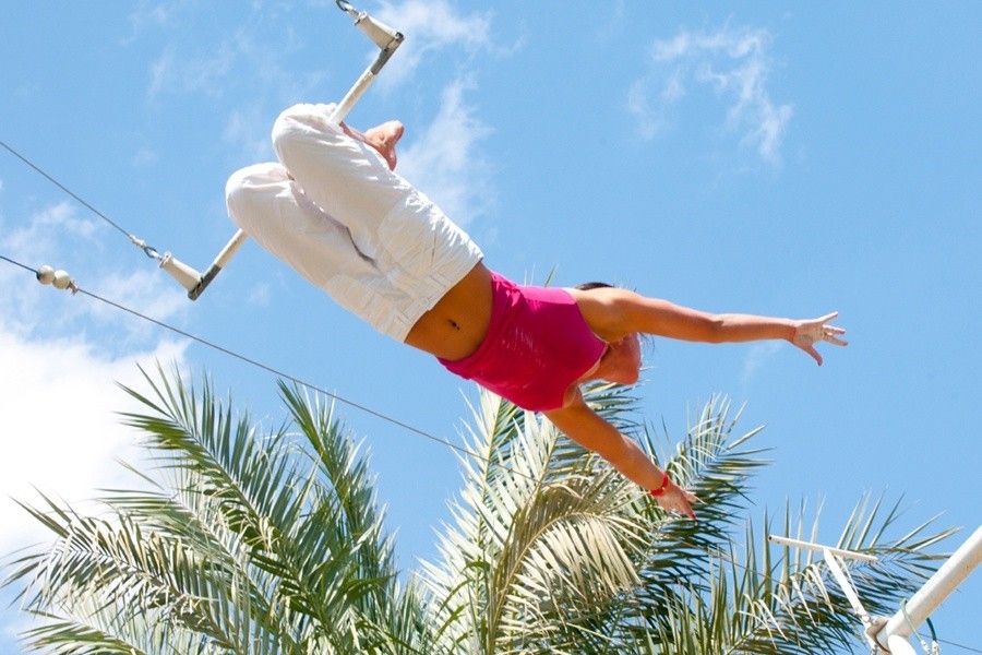 אישה עפה על טרפז בין עצי דקל תחת שמיים כחולים